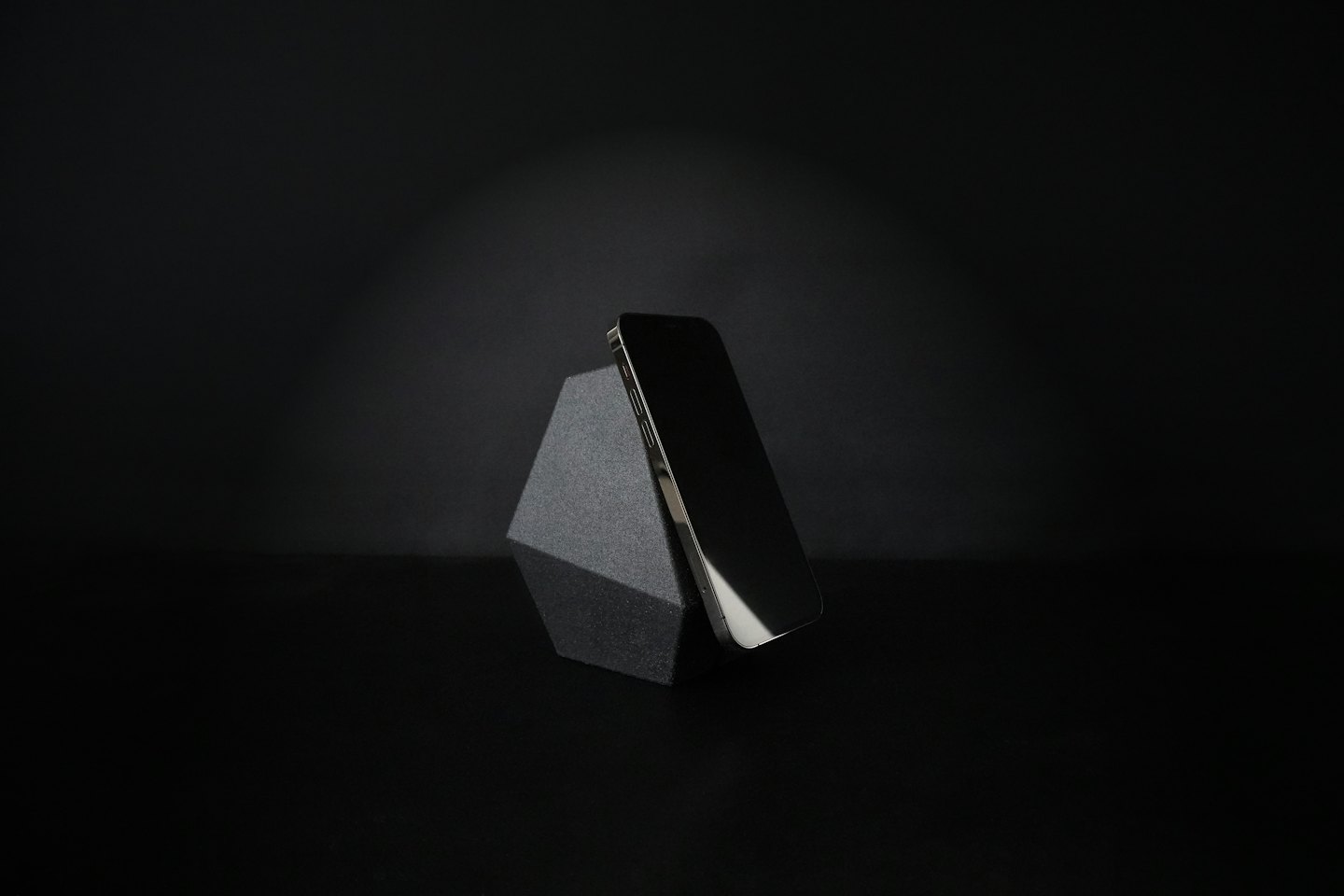 A smartphone leans against a geometric block on a reflective surface.